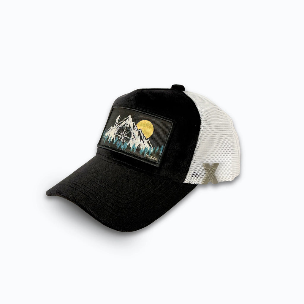 Svart keps i sammet från sidan, som visar den vita nätbaksidan (mesh) och bergskompass-trycket. Unisex truckerkeps från XVERA.

