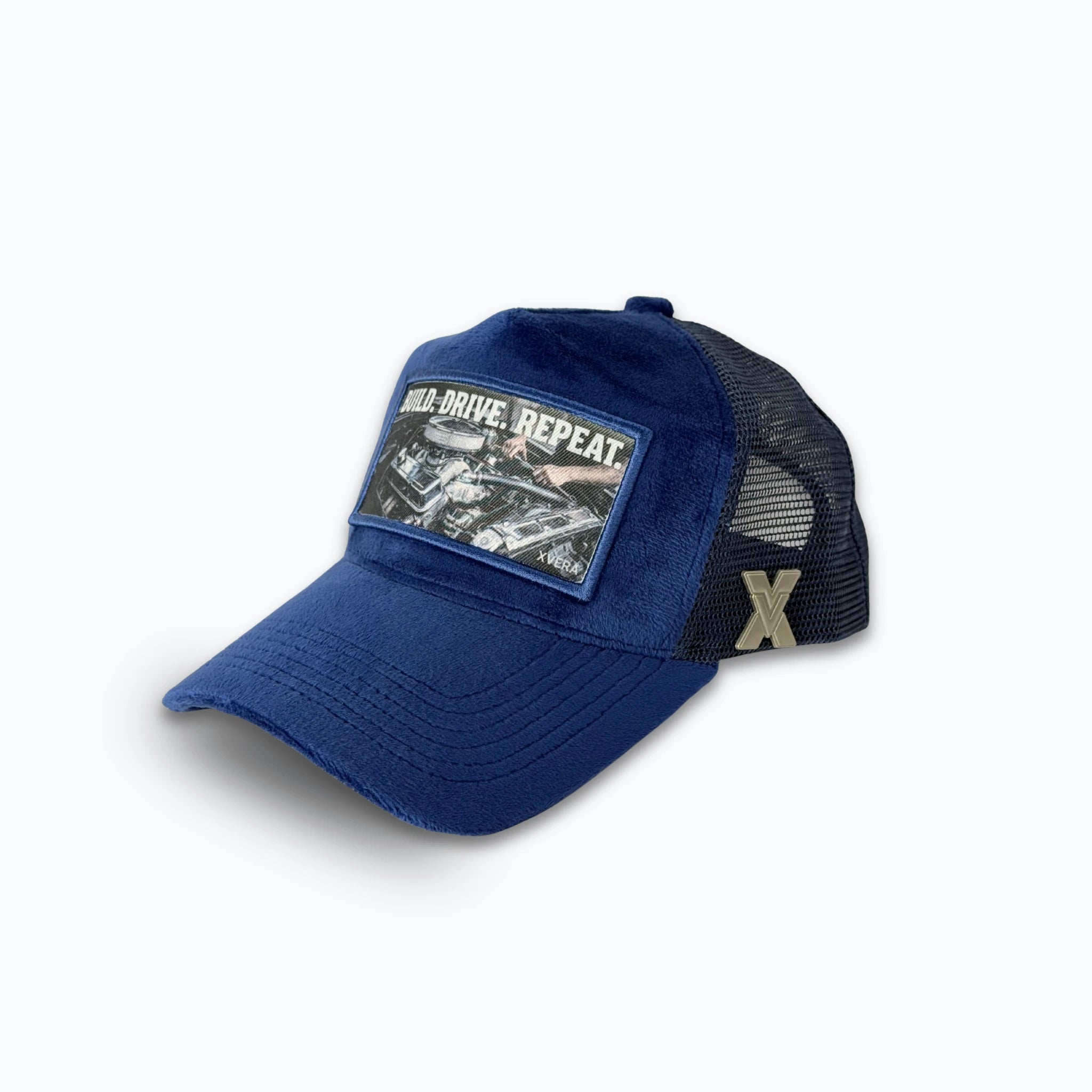 Mörkblå keps i sammet från sidan, som visar den bekväma passformen och BUILD DRIVE REPEAT trycket. Unisex truckerkeps från XVERA.
