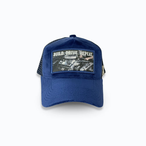 Mörkblå velvet keps framifrån med det vita trycket BUILD DRIVE REPEAT och bilmotiv. Exklusiv truckerkeps för motorintresserade från varumärket XVERA.
