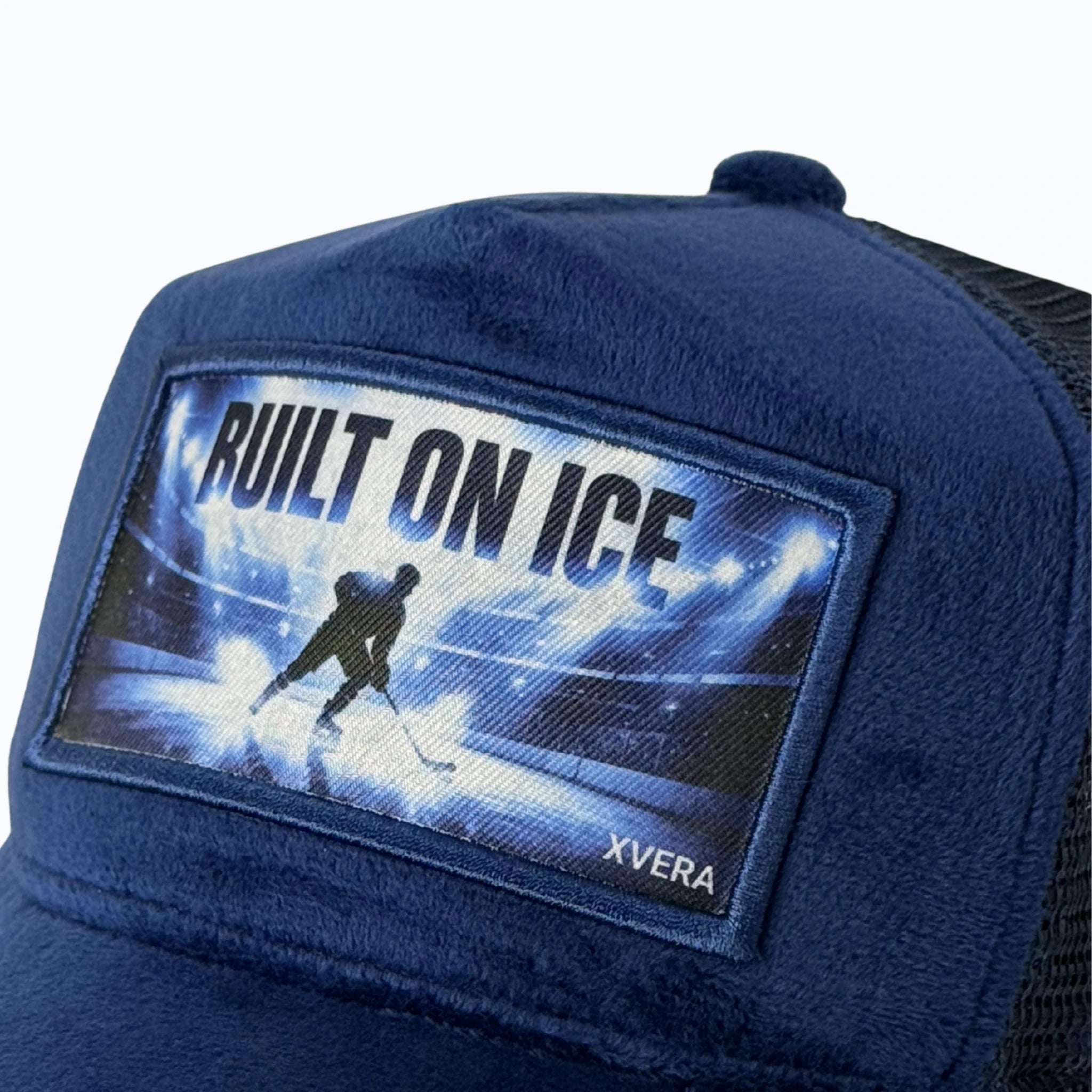 Närbild på det skarpa vita hockeytrycket BUILT ON ICE med klubbor och det exklusiva mörkblå sammetsmaterialet från XVERA.