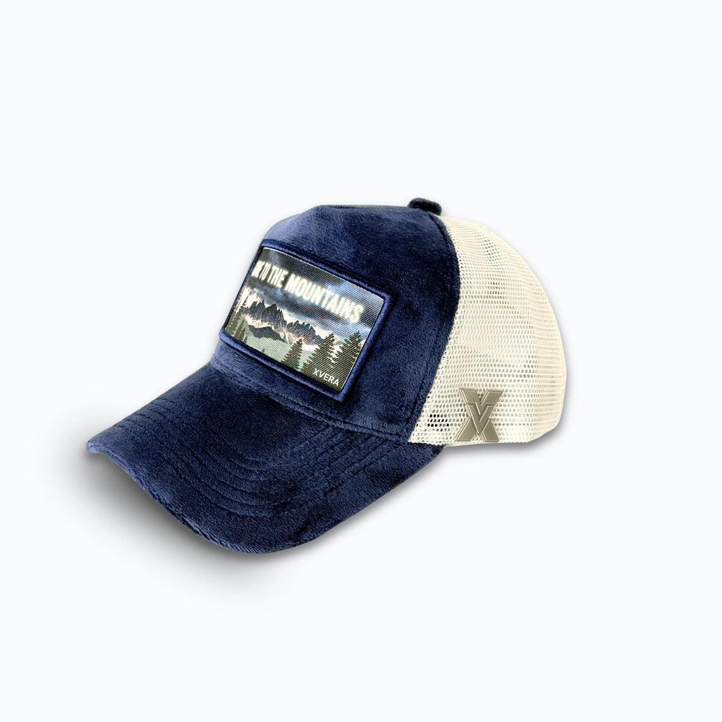 Marinblå keps i sammet från sidan, som visar den cremefärgade nätbaksidan och naturmotivet. Unisex truckerkeps från XVERA.