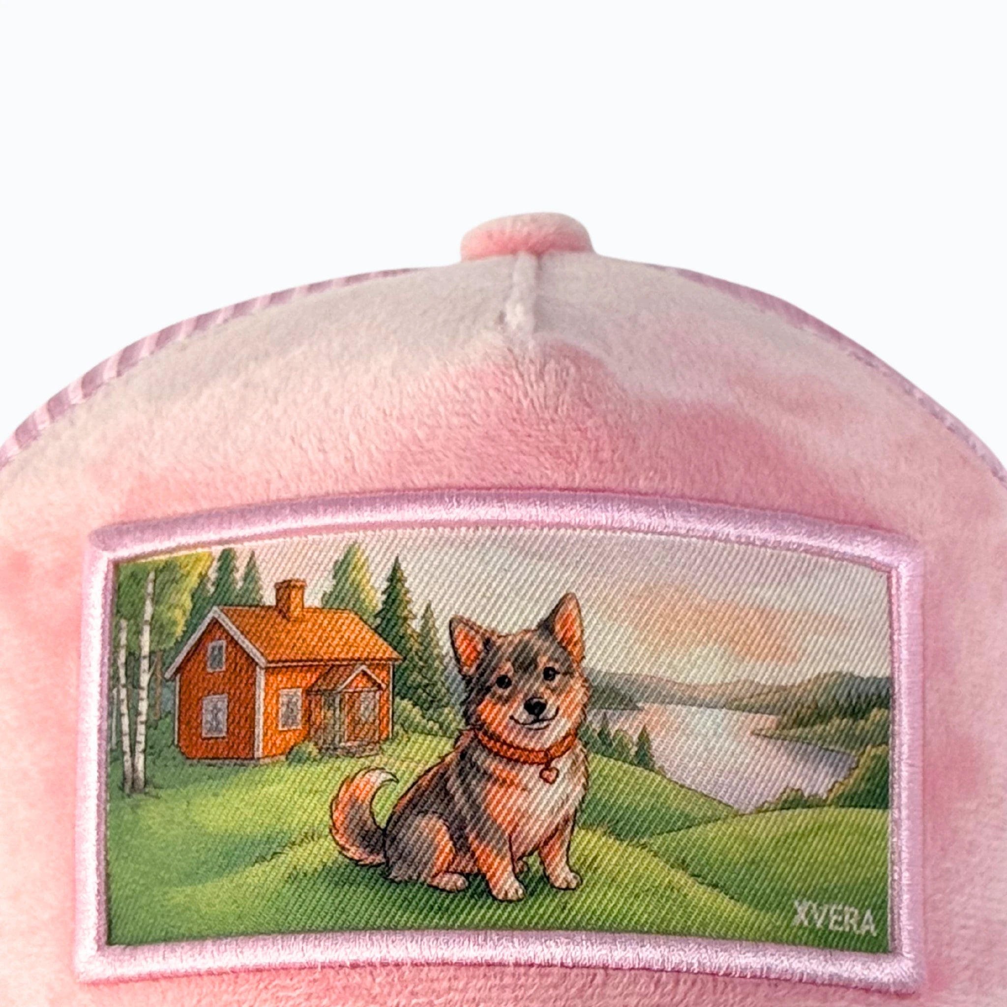 Detaljerad bild på kepsens motiv som visar ett svenskt landskap med hund och stuga på en ljusrosa sammetsbakgrund från XVERA.