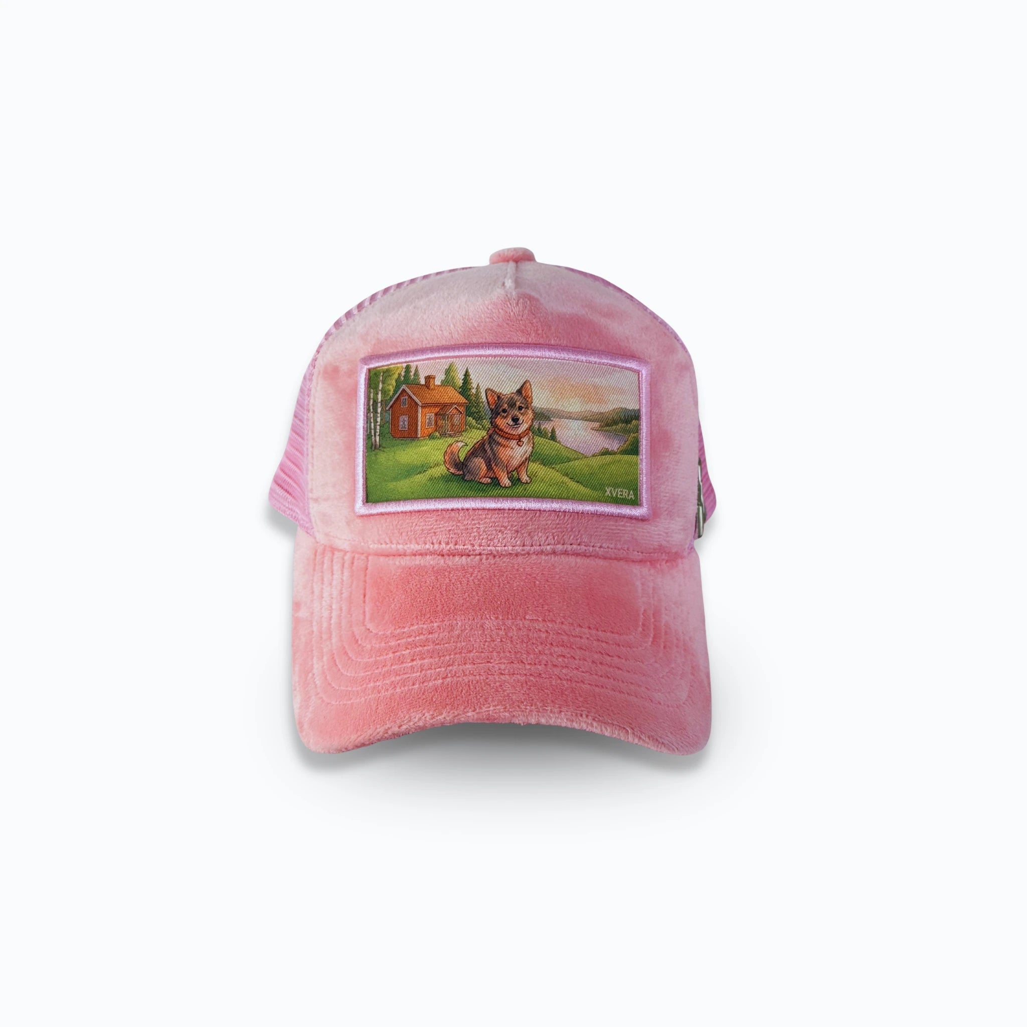 Rosa velvet keps framifrån med ett tryck av en hund framför en röd svensk stuga vid en sjö. Exklusiv truckerkeps från varumärket XVERA.