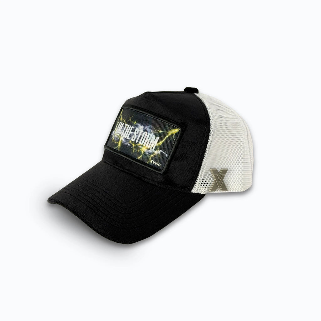 Svart keps i sammet från sidan, som visar den vita nätbaksidan och I AM THE STORM-trycket. Unisex truckerkeps från XVERA.