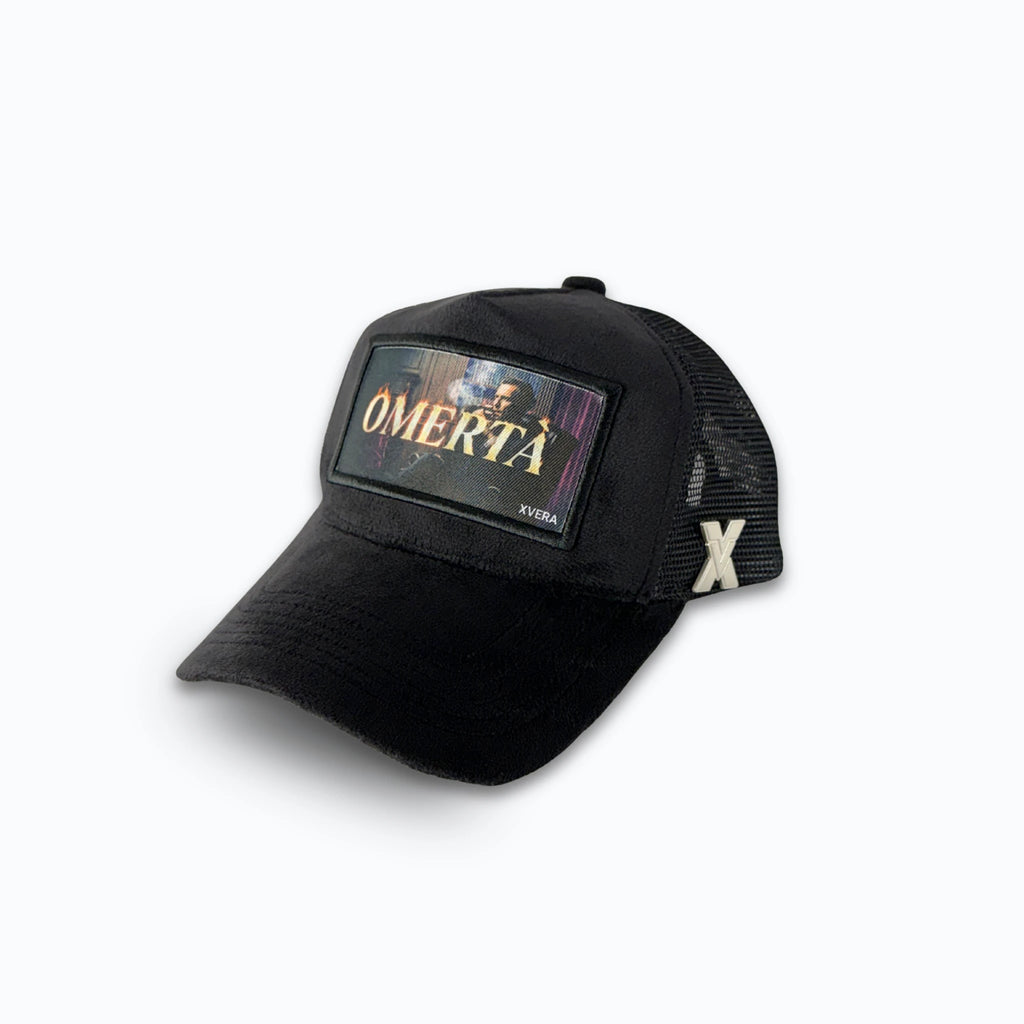 Svart keps i sammet från sidan, som visar passformen och OMERTÀ-trycket. Unisex truckerkeps från XVERA.