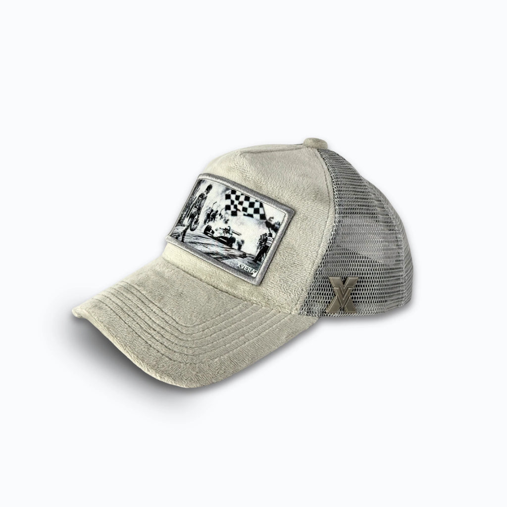 Ljusgrå keps i sammet från sidan, som visar den gråa nätbaksidan och det nostalgiska racingmotivet. Unisex truckerkeps från XVERA.