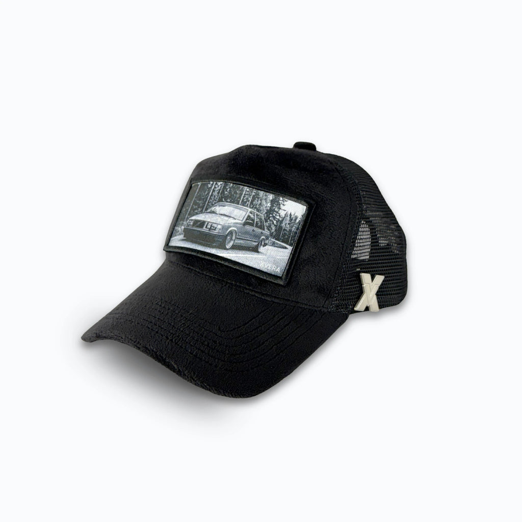 Svart keps i sammet från sidan, som visar den svarta nätbaksidan och det klassiska bilmotivet. Unisex truckerkeps från XVERA.