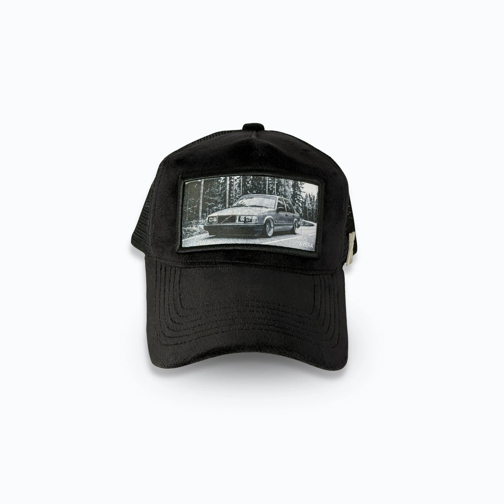 Svart velvet keps framifrån med ett detaljerat svartvitt tryck av en klassisk sänkt Volvo i skogsmiljö. Exklusiv truckerkeps för bilentusiaster från varumärket XVERA.