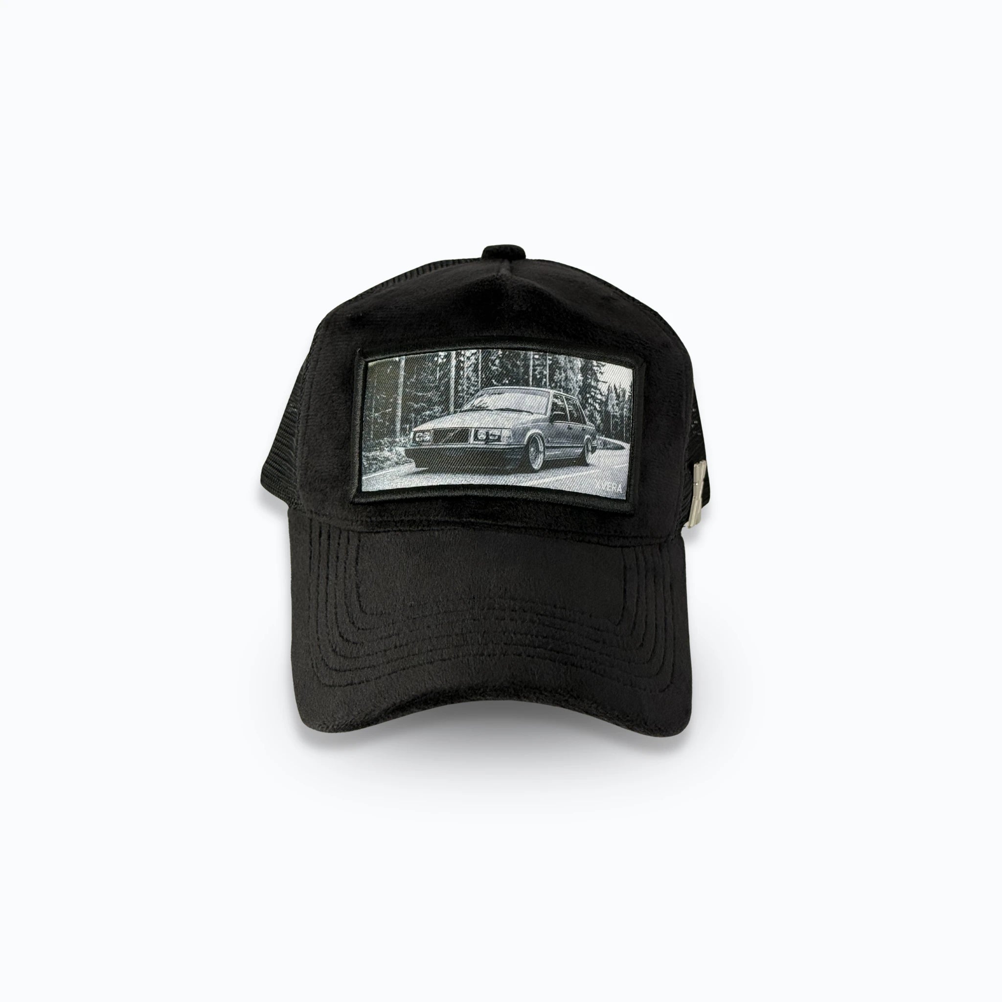 Svart velvet keps framifrån med ett detaljerat svartvitt tryck av en klassisk sänkt Volvo i skogsmiljö. Exklusiv truckerkeps för bilentusiaster från varumärket XVERA.